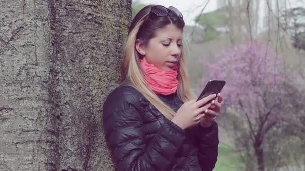 Жінка використовує мобільний телефон у парку — стокове відео