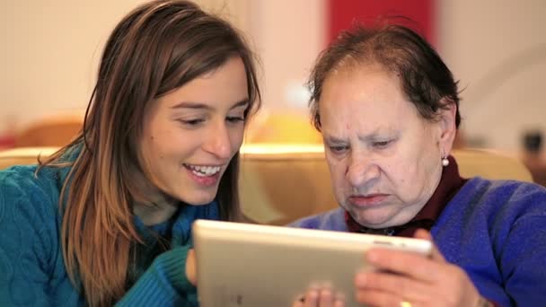 Granddoughter onderwijs zijn grootmoeder met behulp van digitale tablet op Bank — Stockvideo