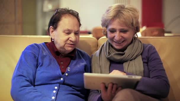 Взрослая женщина дает его матери планшетный компьютер и учит ее использовать его — стоковое видео