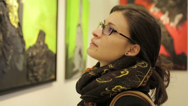 Vista lateral de una hermosa mujer caucásica contemplando obras de arte en un museo de arte — Vídeos de Stock