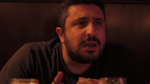 Un mec qui mange et boit un hamburger dans un pub — Video