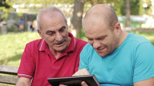 Man lära sin farfar som använder TabletPC på park — Stockvideo