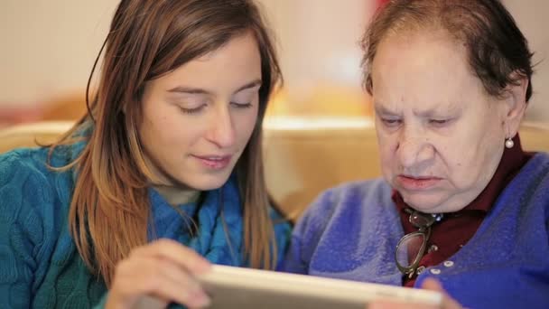 Granddoughter undervisning hans mormor med digital tablett på soffan — Stockvideo