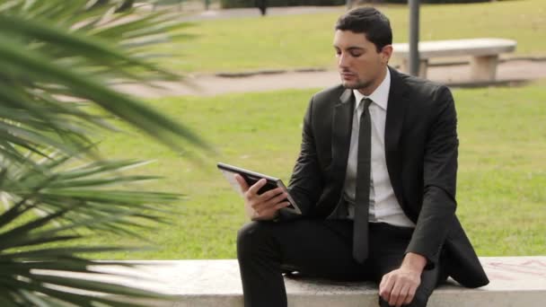 Podnikatel v parku s tabletem, sedí na lavičce — Stock video