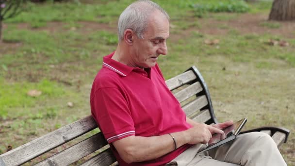 Homem idoso aposentado descansando e usando seu tablet à mesa no parque — Vídeo de Stock