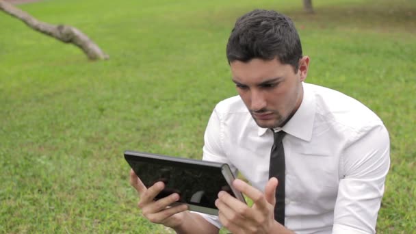 Hombre de negocios sentado debajo del árbol usando tableta — Vídeos de Stock