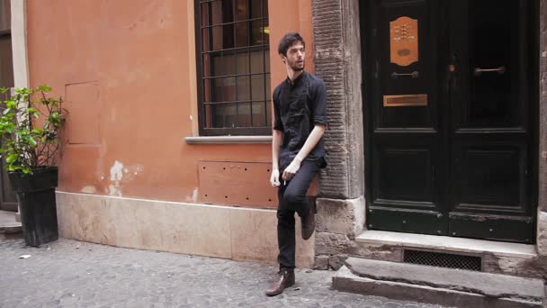 One twenties young man leaning on a wall outdoors in grungy setting — Stock Video