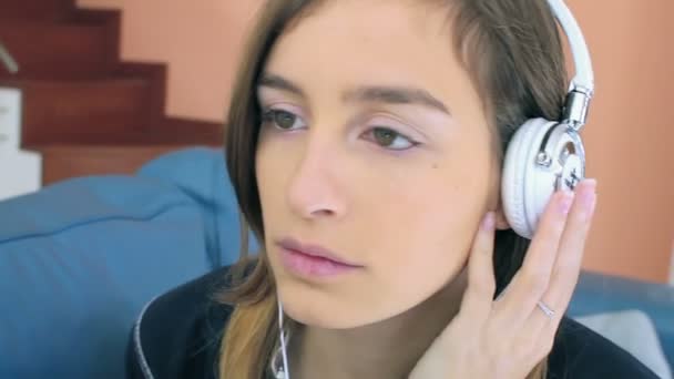 Menina bonita gosta de ouvir música em fones de ouvido enquanto deitado no sofá — Vídeo de Stock