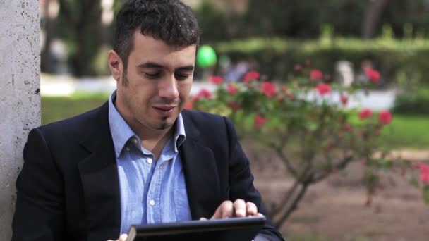 Joven hombre de negocios con Tablet PC en el parque mirando a la cámara — Vídeos de Stock