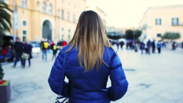 La parte de atrás es una chica caminando por la calle de la ciudad. Al final sonríe — Vídeos de Stock