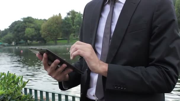 Homem de negócios usando um dispositivo tablet digital enquanto em pé em um parque clássico — Vídeo de Stock
