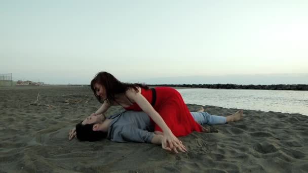 Молодая привлекательная пара влюблённая целуется на пляже вечером — стоковое видео