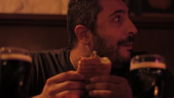 Un mec qui mange et boit un hamburger dans un pub — Video