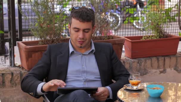 Young businessman working on tablet computer in cafe drinking a beverage — Stock Video