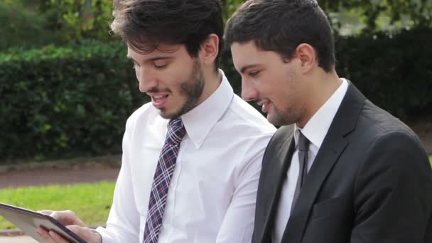 Deux hommes d'affaires regardant la tablette sur un banc de parc — Video