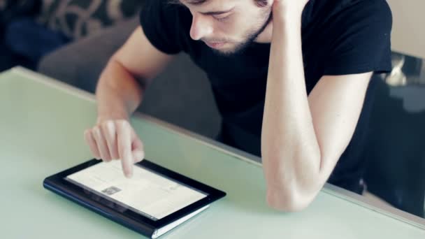 Молодой человек учится на стопке книг на столе с планшетом — стоковое видео