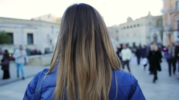 Вид сзади на молодую женщину, идущую по улице — стоковое видео