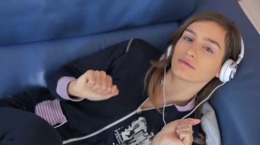 Mutlu genç kadın dinlemek için müzik kulaklıklar kanepede