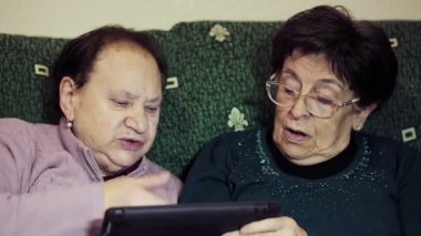 Yaşlı kadınlar evde birlikte oturup tablet bilgisayar kullanıyorlar.