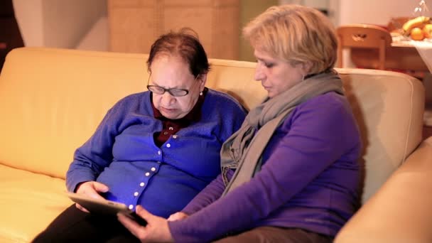 Доросла жінка дає матері планшетний ПК і навчає її ним користуватися — стокове відео