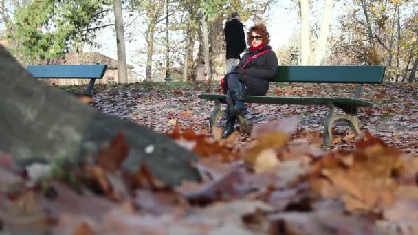 Kvinnan sitter på en bänk i parken — Stockvideo
