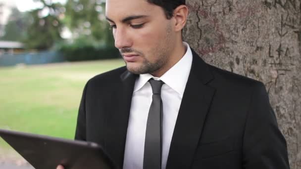 Hombre de negocios usando tableta digital en el parque frente a un lago — Vídeo de stock