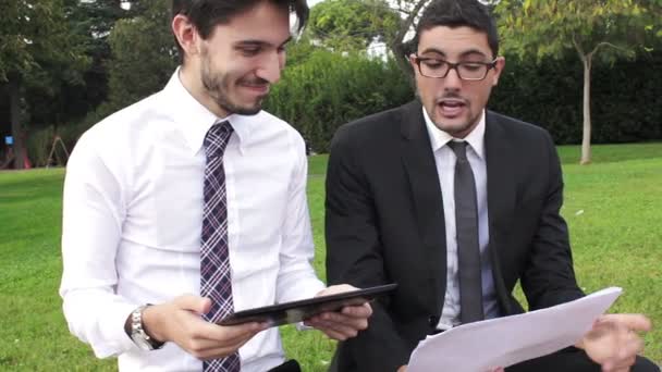 Два бизнесмена с планшетом и ноутбуком говорят о проекте в парке — стоковое видео