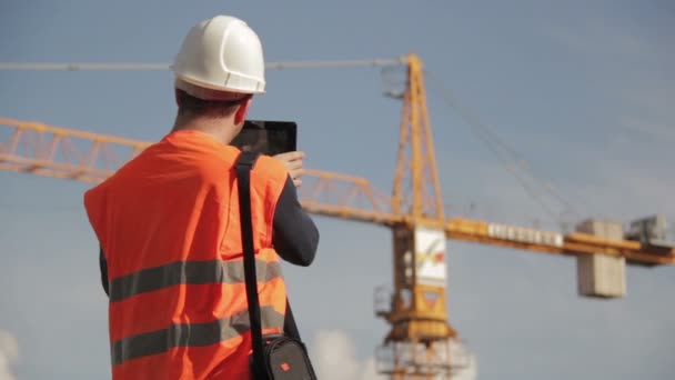 Bauingenieur trägt Warnweste mit gelbem Kran im Hintergrund — Stockvideo