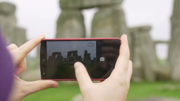 young woman making photos with smartphone to Stonehenge