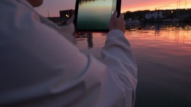 Κάνοντας φωτογραφία με ένα tablet στο ηλιοβασίλεμα κοντά στον ποταμό — Αρχείο Βίντεο