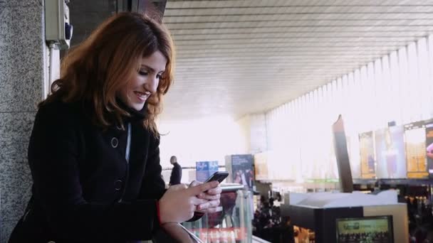 Mulher usando um telefone celular dentro de uma estação de trem enquanto espera o trem — Vídeo de Stock