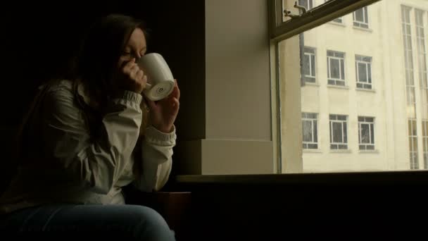 Doordachte jongedame koffie drinken in de buurt van het venster — Stockvideo