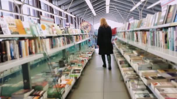 Mulher andando entre as prateleiras de uma livraria — Vídeo de Stock