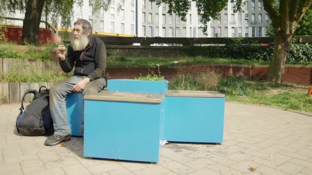 Bezdomny siedzi w mieście i palenie — Wideo stockowe