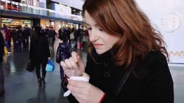Mujer comiendo un helado dentro de una estación de tren mientras espera el tren — Vídeos de Stock