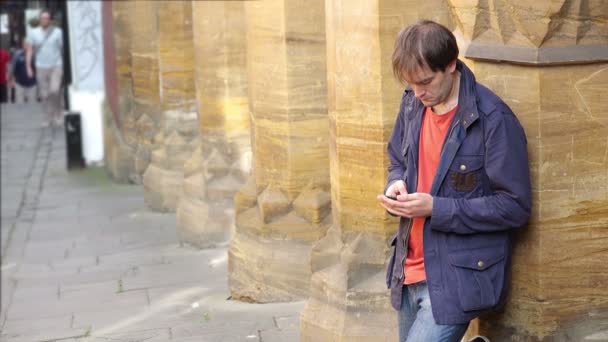 Joven escribiendo un mensaje con el teléfono inteligente de pie en la acera — Vídeo de stock