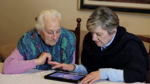 Dos ancianas están utilizando la tableta en casa. 80, 70, abuela, anciano, antiguo — Vídeos de Stock