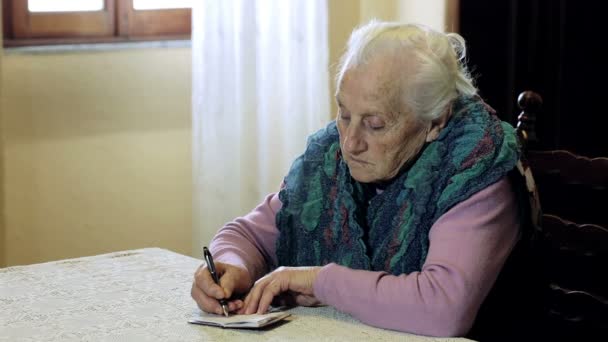 Old woman is writing on little notepad: pen, paper, older, ancient, notes, takes — Stock Video