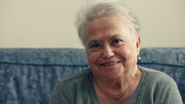 La anciana sentada en el sofá mirando a la cámara se ríe con estruendo — Vídeos de Stock