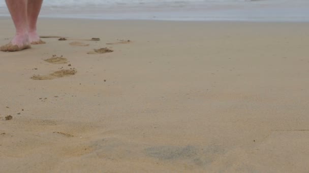 Pies de hombre joven caminando sobre la arena en la playa en un día lluvioso — Vídeo de stock