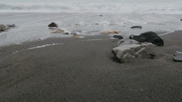 Día lluvioso en la playa, las olas rompiendo en la arena y las rocas — Vídeo de stock