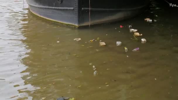 Flytande sopor nära en båt förtöjd i en kanal — Stockvideo