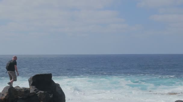Портрет молодого человека, взбирающегося на скалу и смотрящего на бурное море — стоковое видео