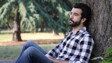 Genç adam parkta çimlerin üzerinde oturuyor.