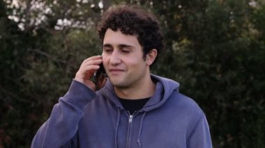 Teknoloji, sohbet. Genç rahat adam parkta cep telefonuyla konuşuyor.