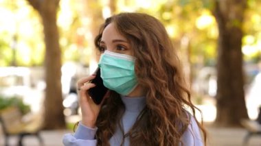 Maskeli genç bir kadın maske takarak mobie 'siyle konuşuyor.