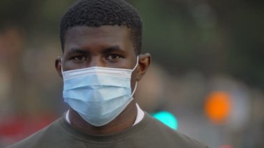 Maske takan düşünceli siyah adam kameraya yaklaşıyor ve ona bakıyor. 