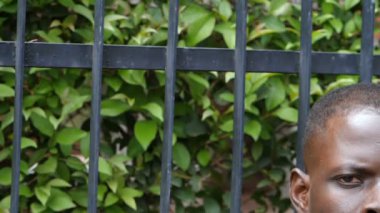 Arkaplanda kamera ızgarasına bakan esaret derecesinde ciddi siyahi adamın sembolü