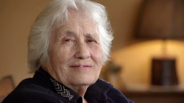 Yaşlı kadın başını sallıyor ve kameraya gülümsüyor.