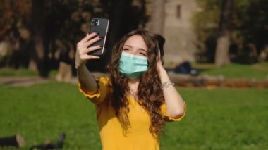Maskeli selfie. Parktaki kız selfie çekip kameraya gülümsüyor.